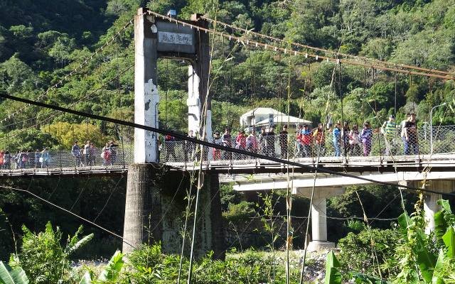 Visitors crossing the Neiwan suspension bridge among green trees