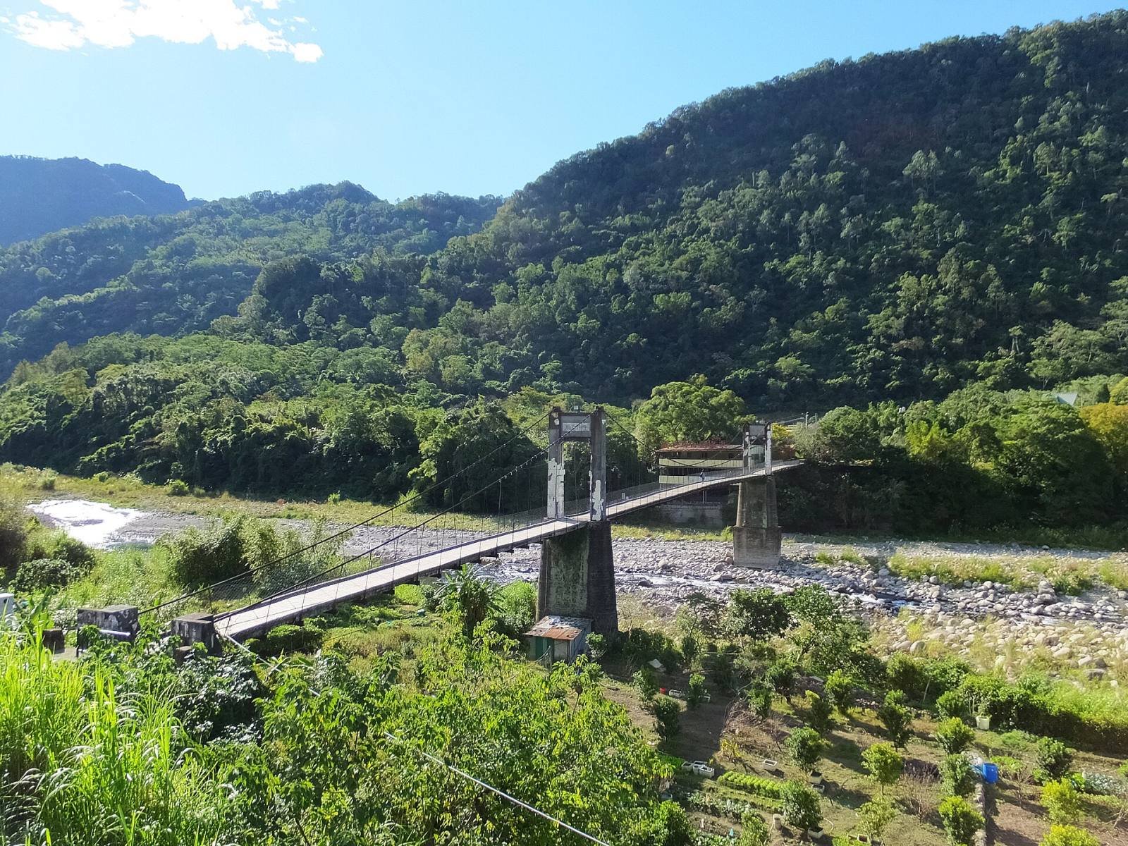 The Neiwan suspension bridge across a wide river valley, below forested hills