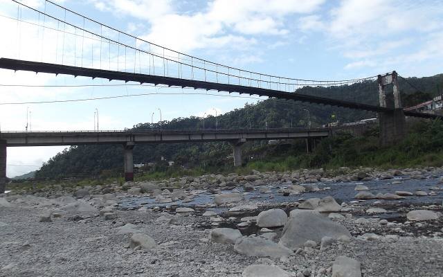 The Neiwan suspension bridge over a rocky river, with green hills behind